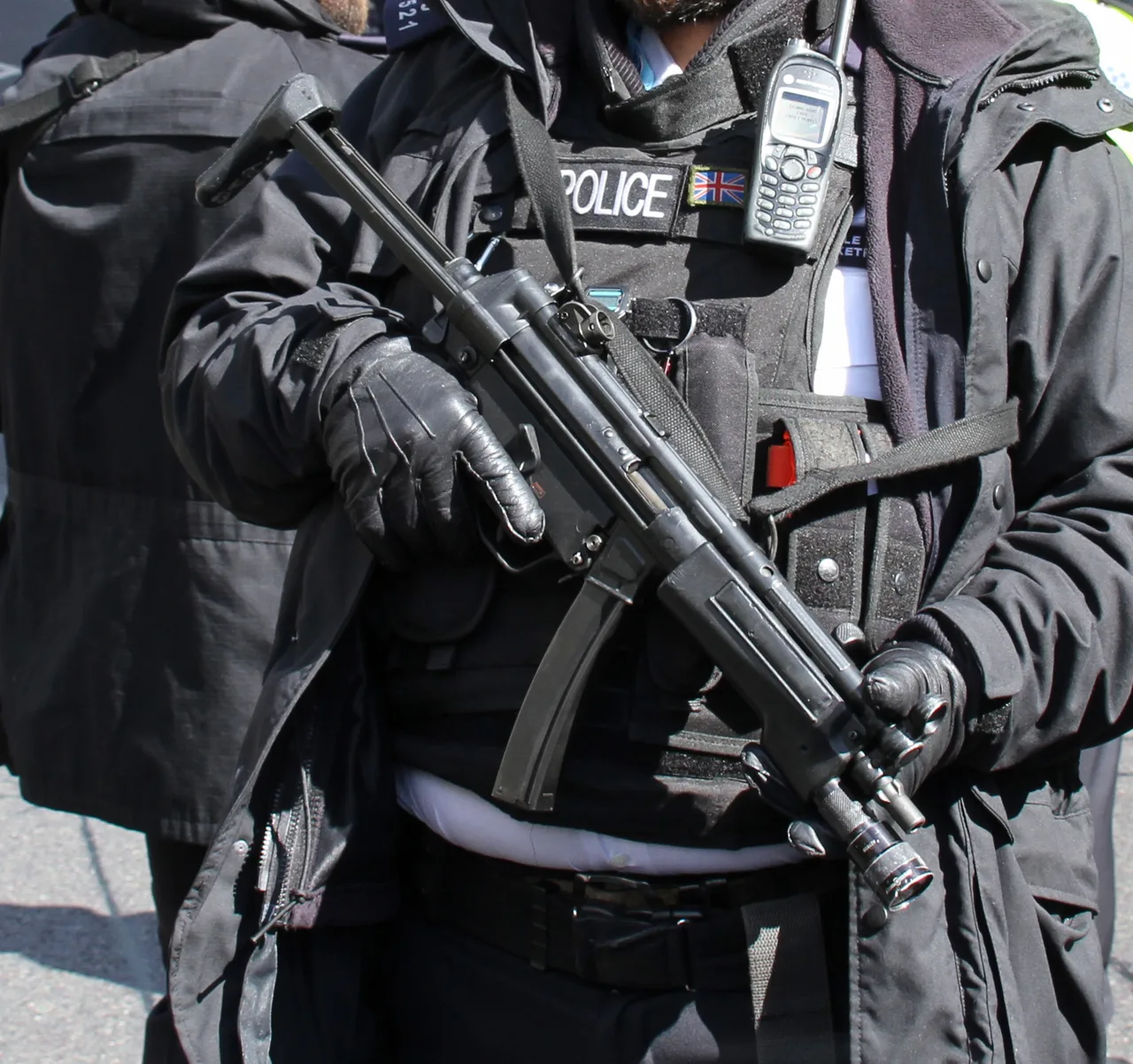 Полицейский в перчатках держит Heckler & Koch MP5 с подствольным фонарём — реальный прообраз MP5A4 из Rust